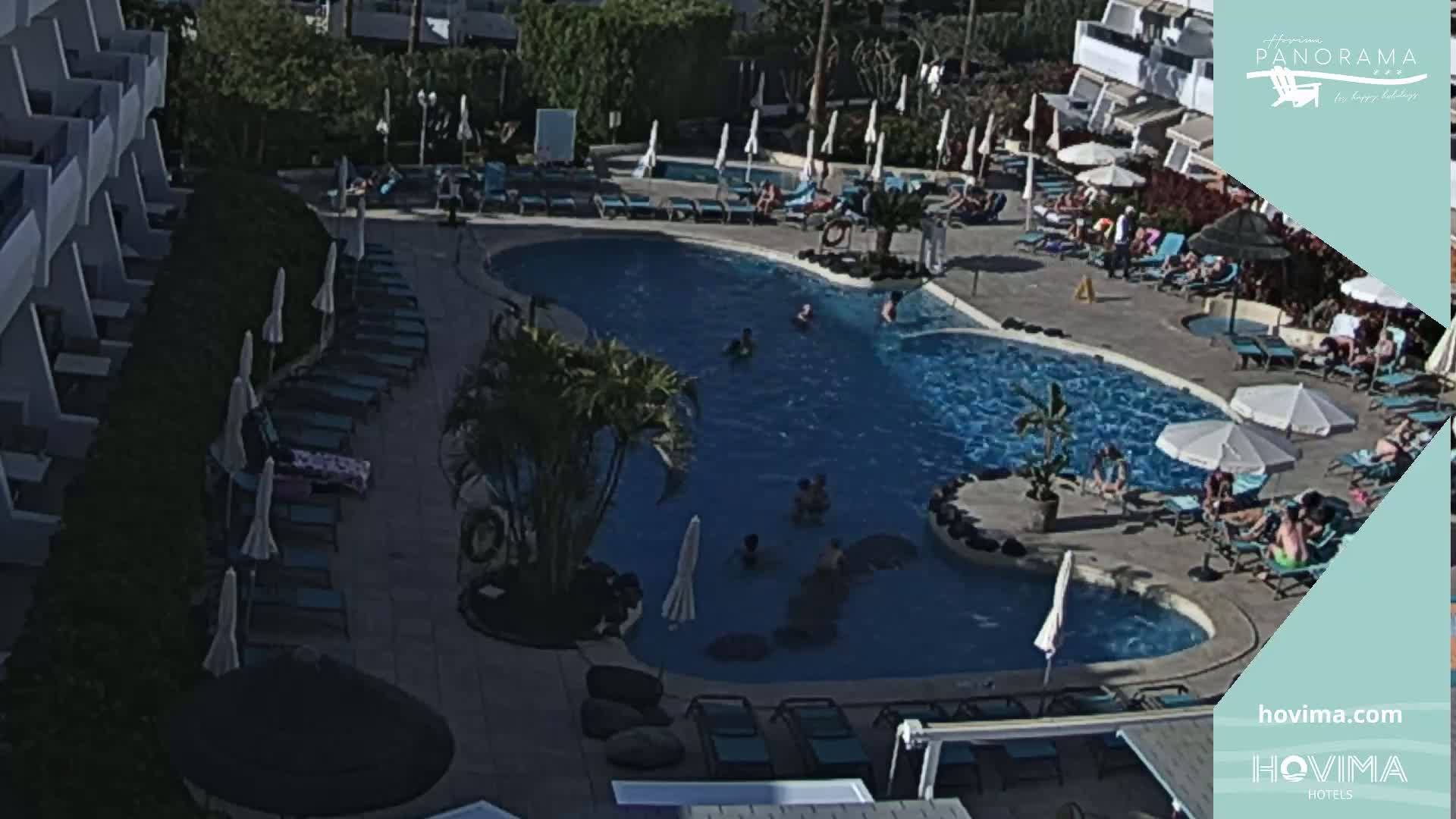 A resort pool with numerous people relaxing and swimming in sunny weather.