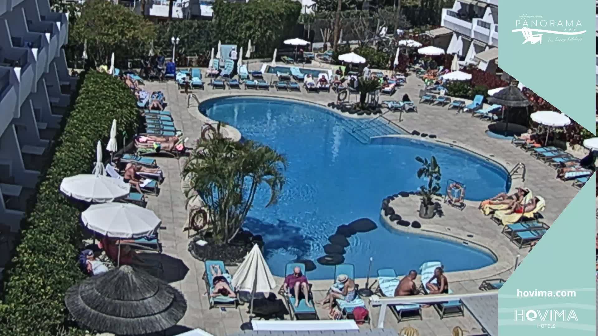 A kidney-shaped swimming pool surrounded by sunbathers and lounge chairs on a sunny day.