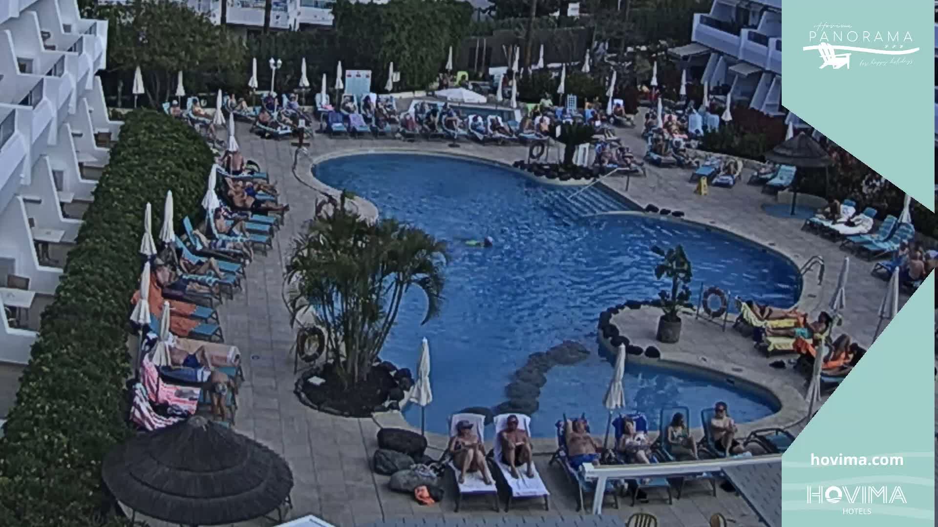 An outdoor pool surrounded by lounge chairs and people relaxing in the sun.