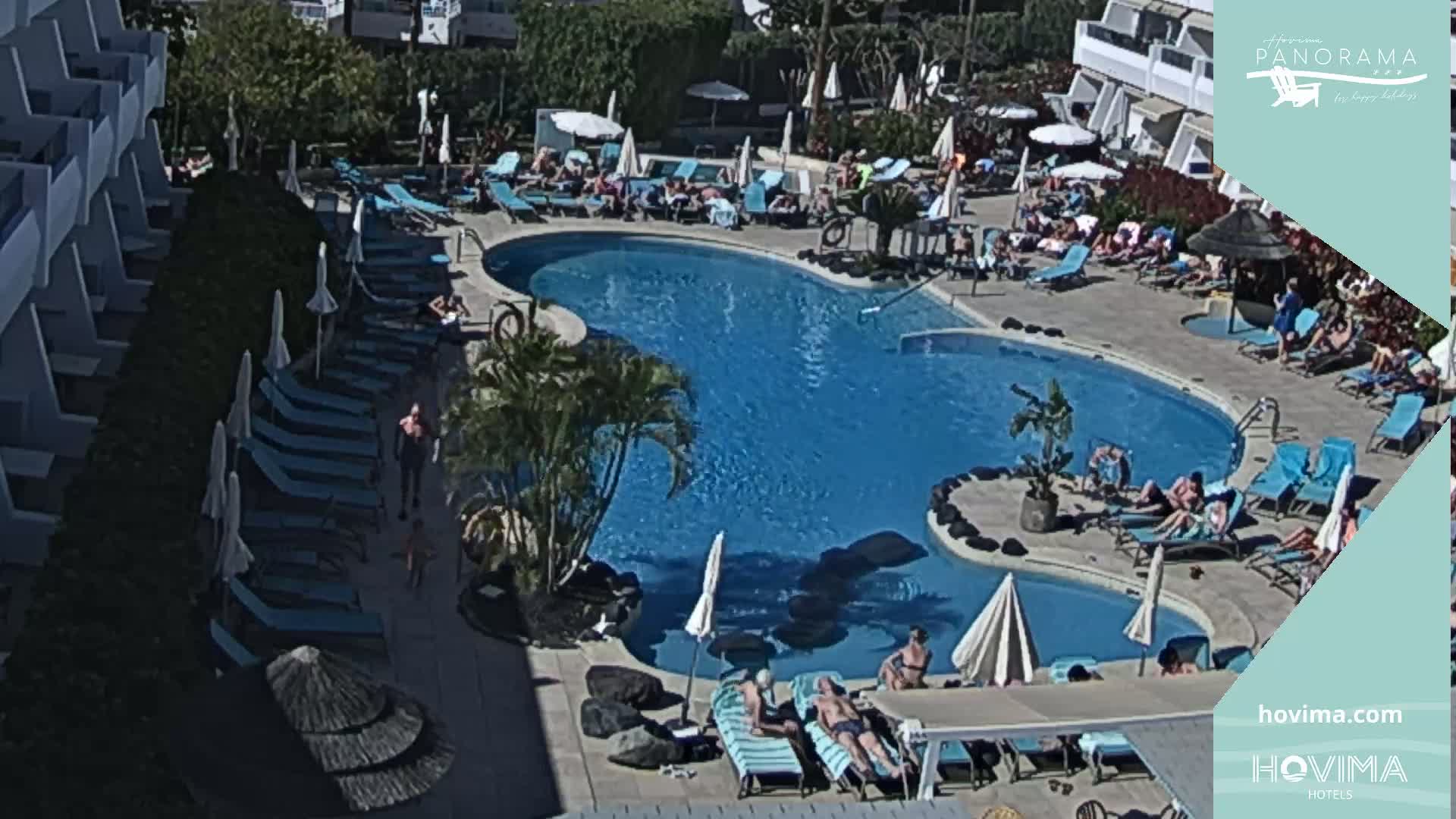 An outdoor pool with many people lounging on chairs and in the water on a sunny day.