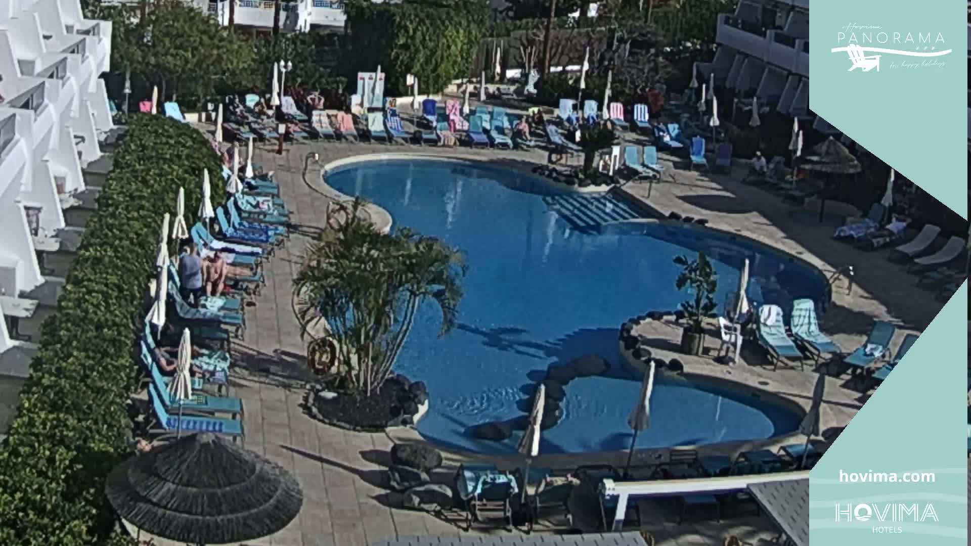 A resort pool with surrounding lounge chairs and umbrellas under a sunny sky.
