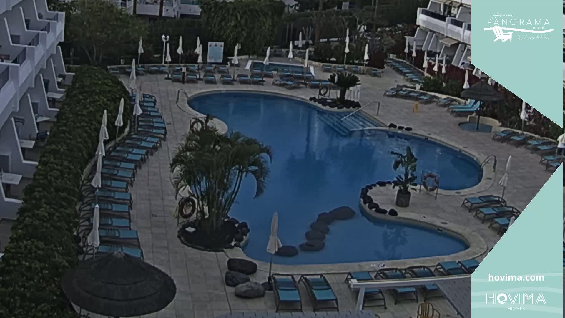 An outdoor swimming pool with surrounding lounge chairs and umbrellas, situated next to a hotel building.