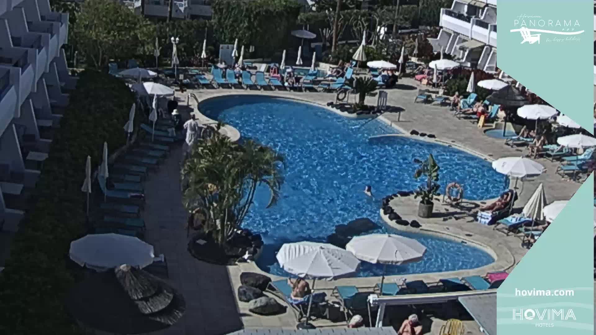 An outdoor pool with many people lounging around it on a sunny day.
