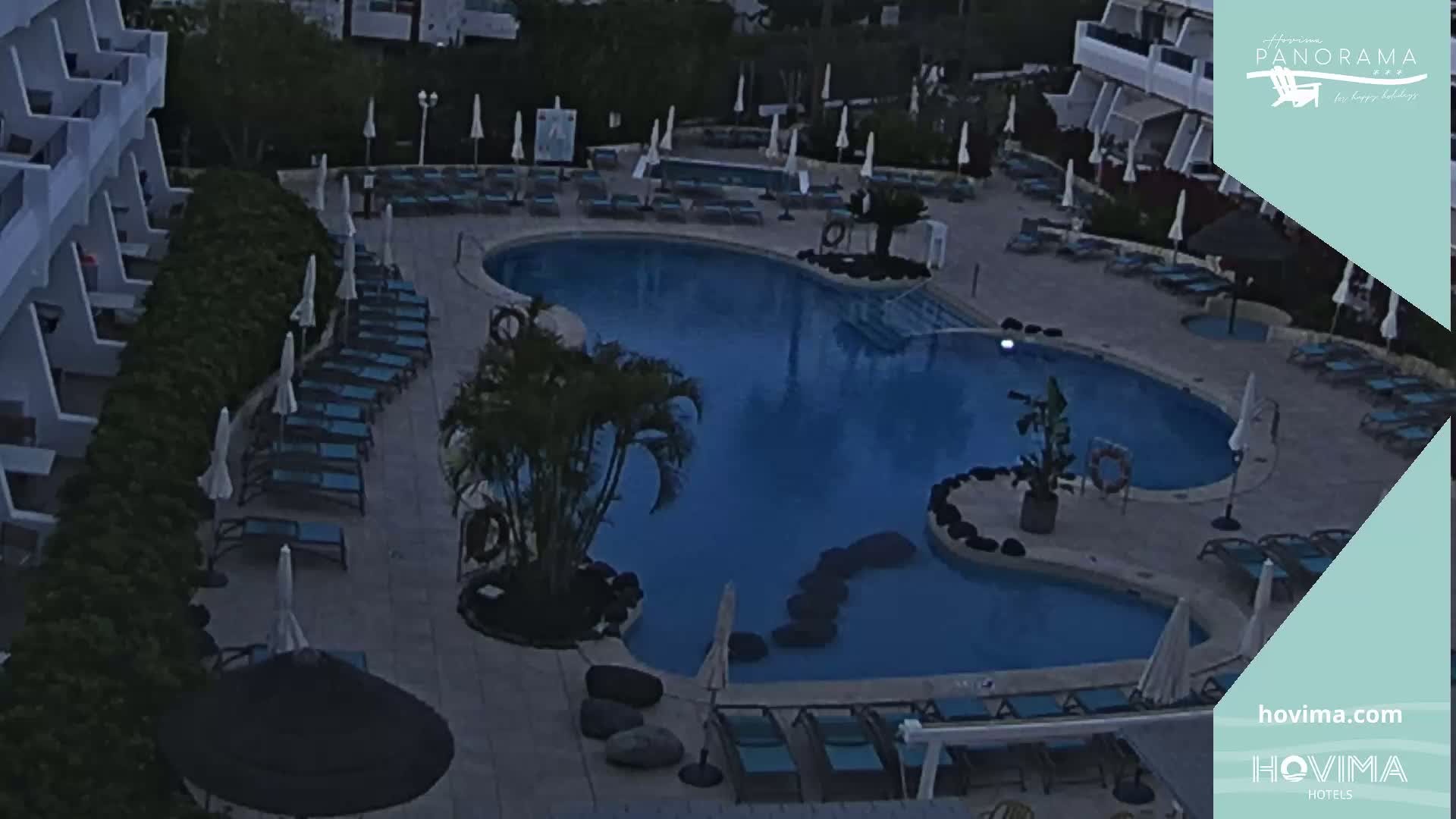 An outdoor pool area with lounge chairs and umbrellas under a dark sky.