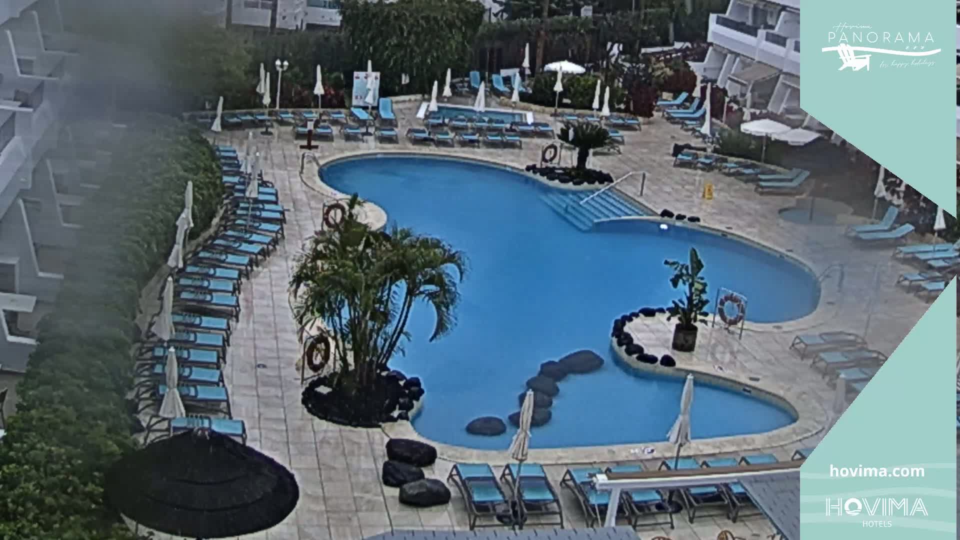 An outdoor pool with surrounding lounge chairs and umbrellas is partially obscured by an overcast sky.