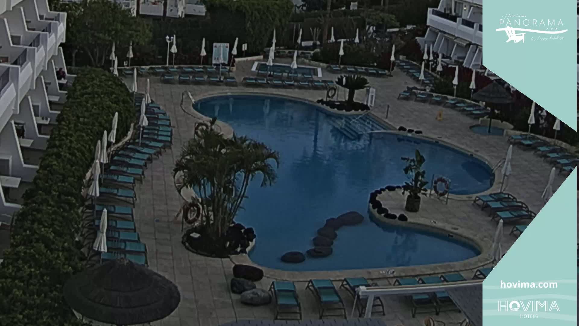 An outdoor swimming pool surrounded by lounge chairs and umbrellas, situated next to a building.