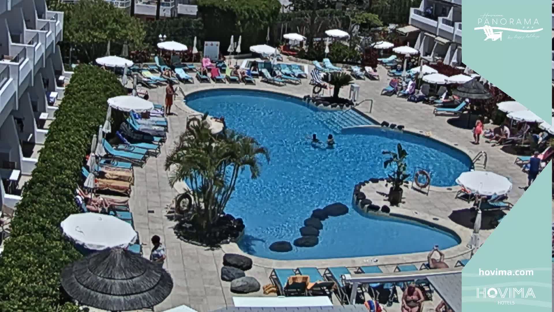 A resort pool area with numerous lounge chairs and umbrellas surrounding a kidney-shaped swimming pool on a sunny day.