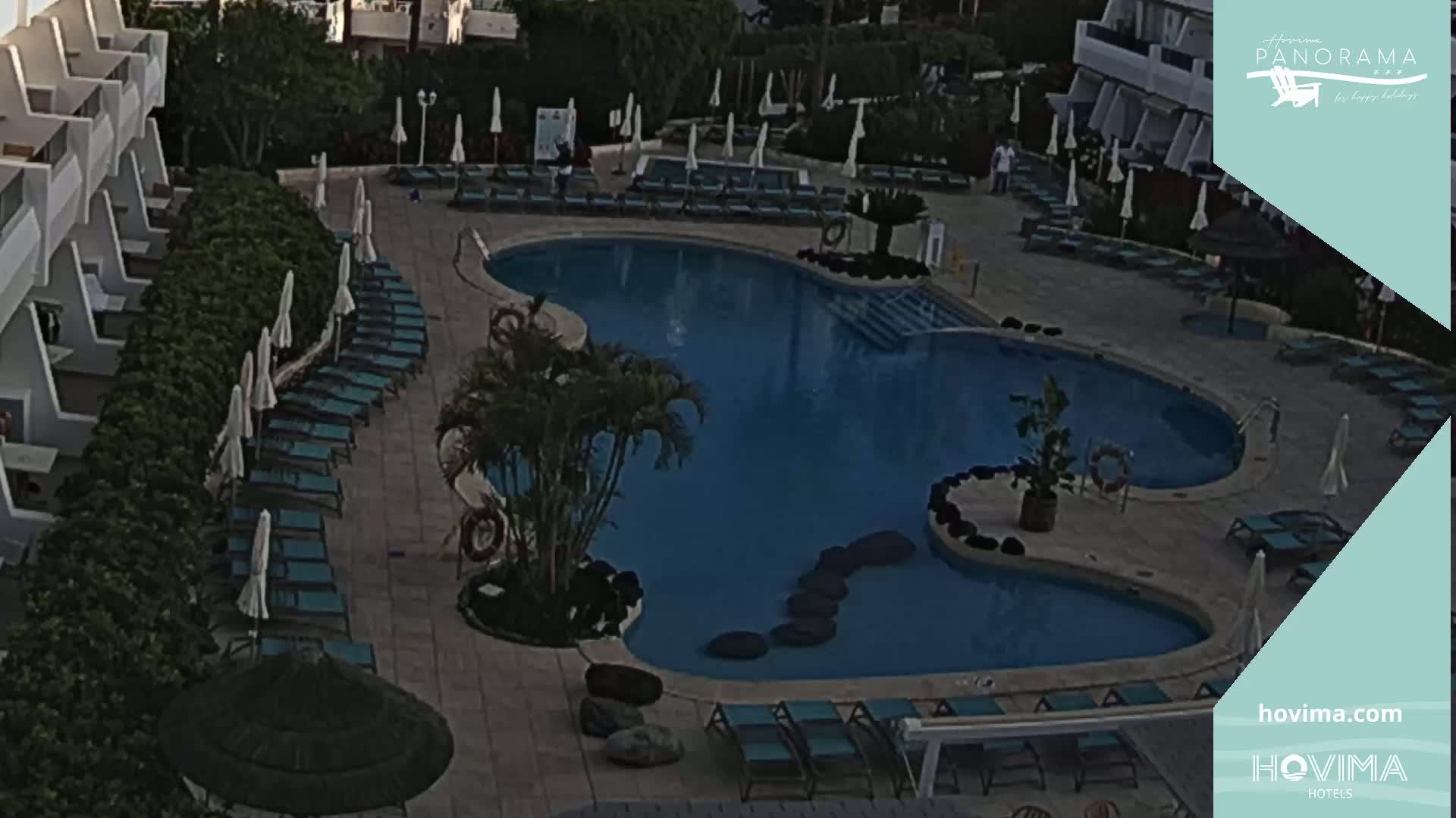An outdoor swimming pool with surrounding lounge chairs and umbrellas at dusk or dawn.