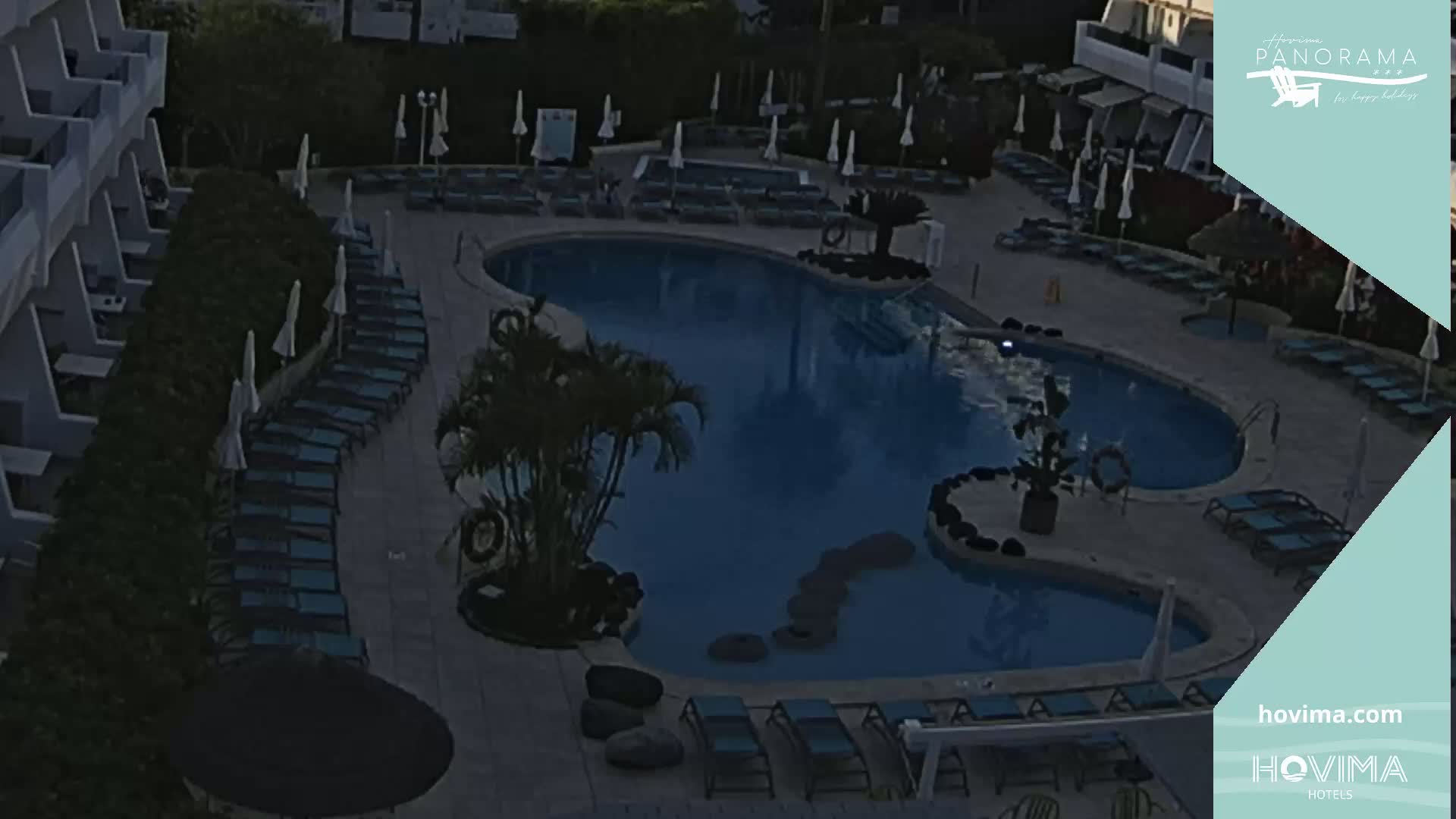 An outdoor swimming pool with surrounding lounge chairs and umbrellas at dusk.