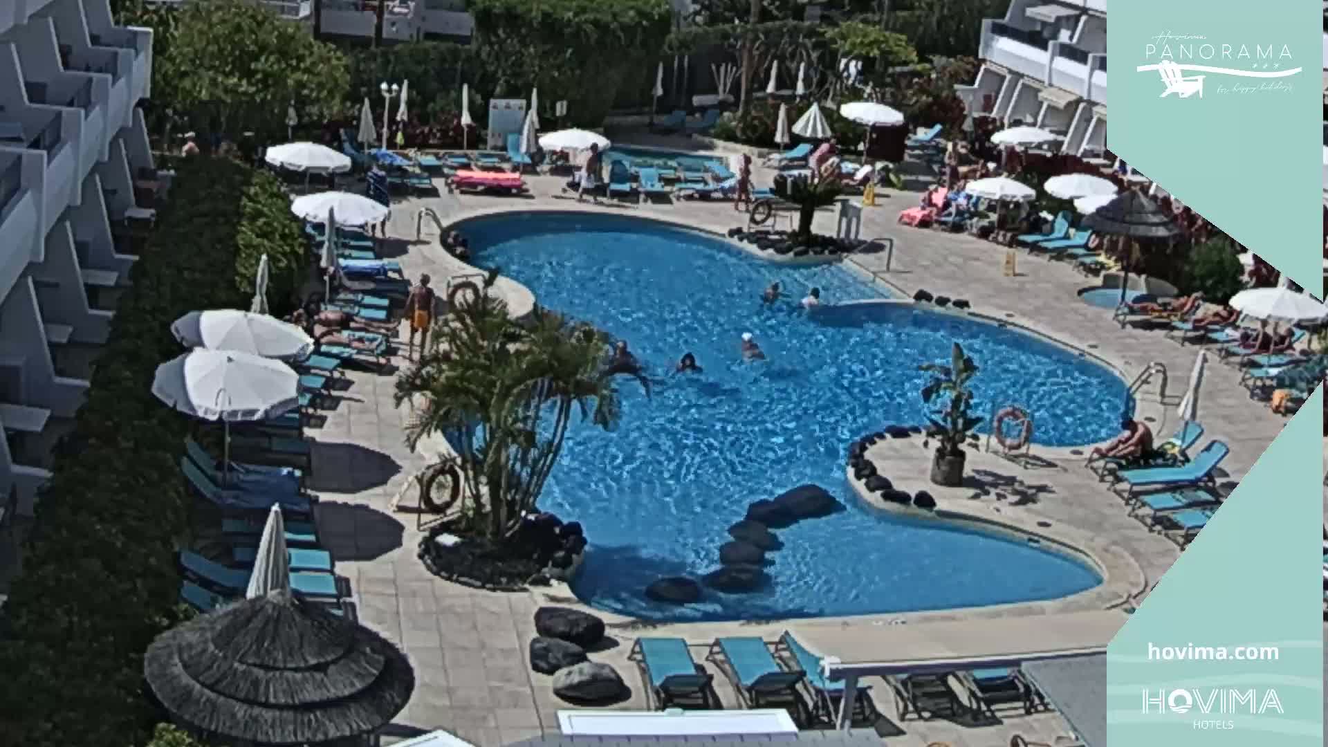 A large, freeform swimming pool surrounded by lounge chairs and umbrellas, in a sunny outdoor resort setting.