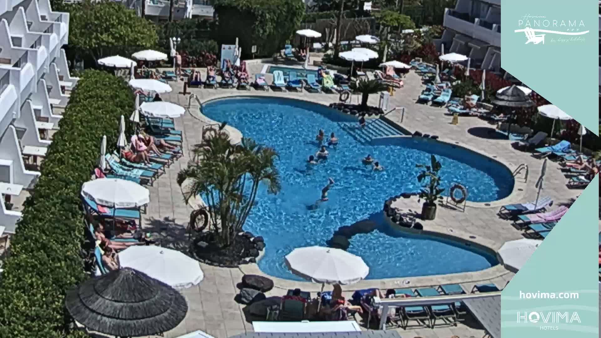 A resort pool area with many people lounging by the pool and swimming on a sunny day.