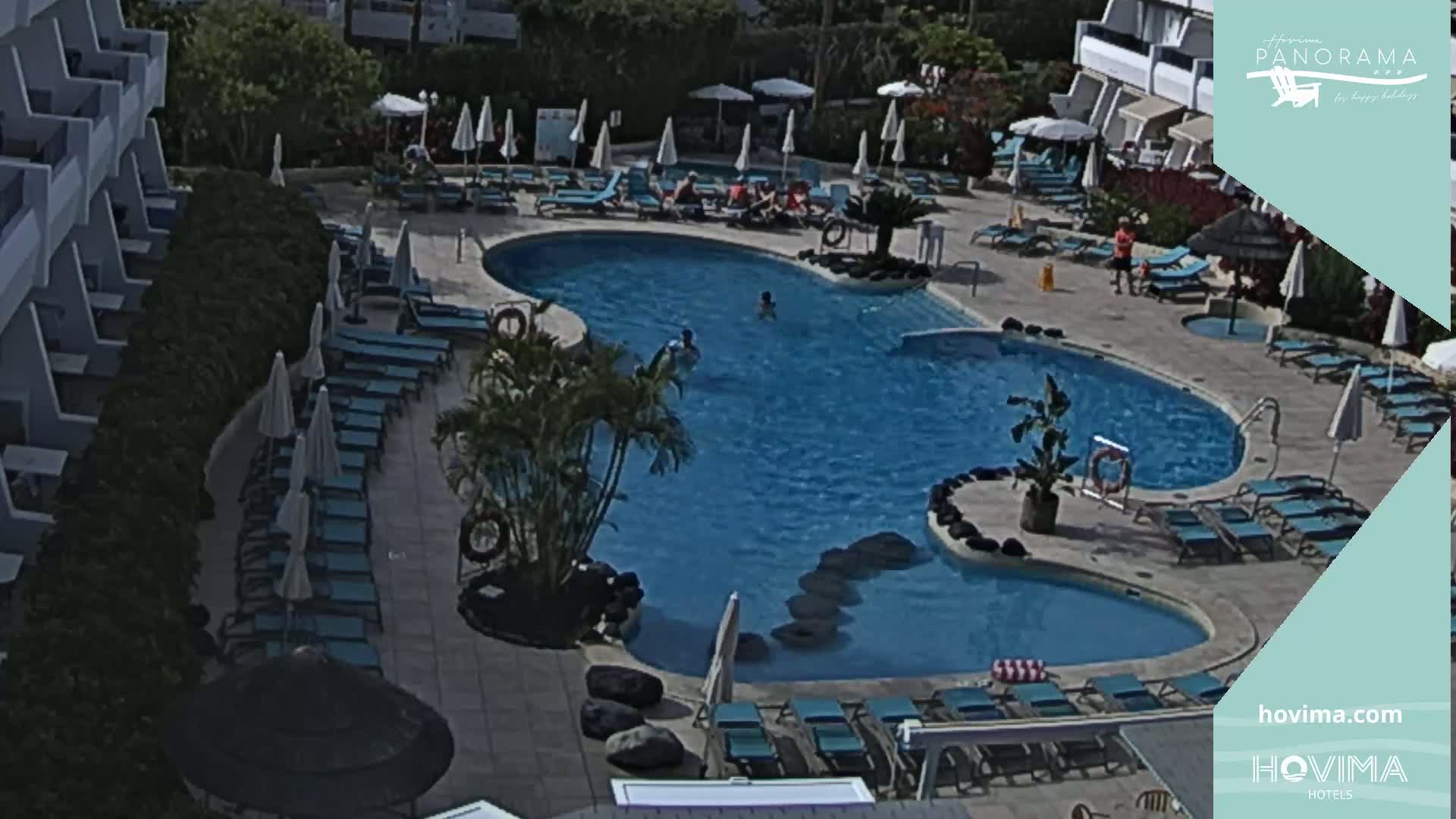An outdoor swimming pool with surrounding lounge chairs and umbrellas on a sunny day.