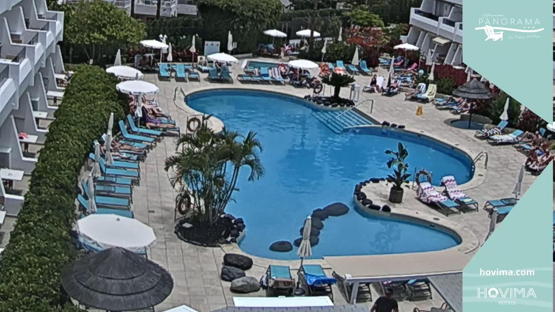 A kidney-shaped swimming pool surrounded by lounge chairs and umbrellas on a sunny day.