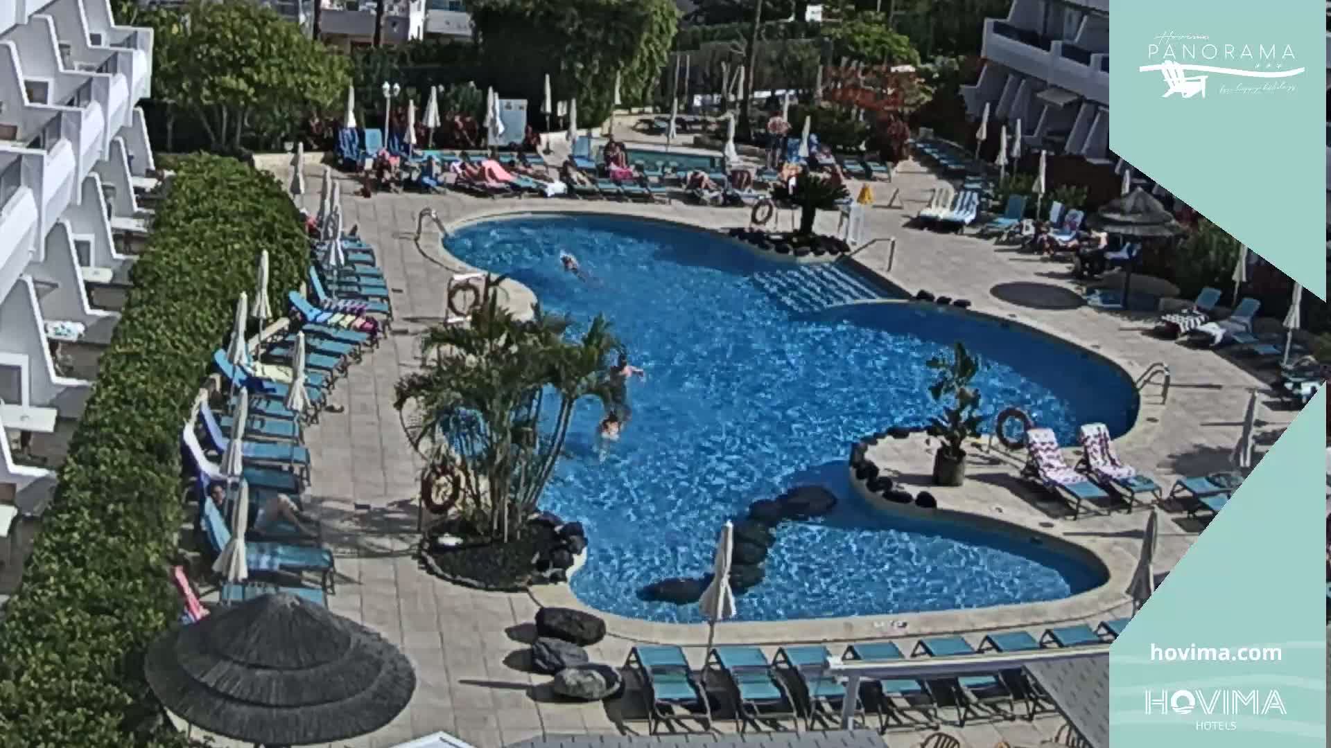 An outdoor swimming pool surrounded by lounge chairs and umbrellas on a sunny day.