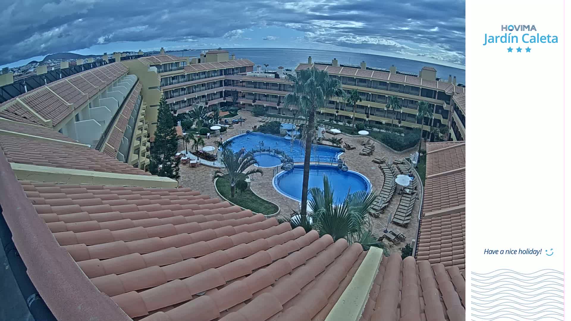 An overhead view of a resort pool area with multiple buildings under a cloudy sky.