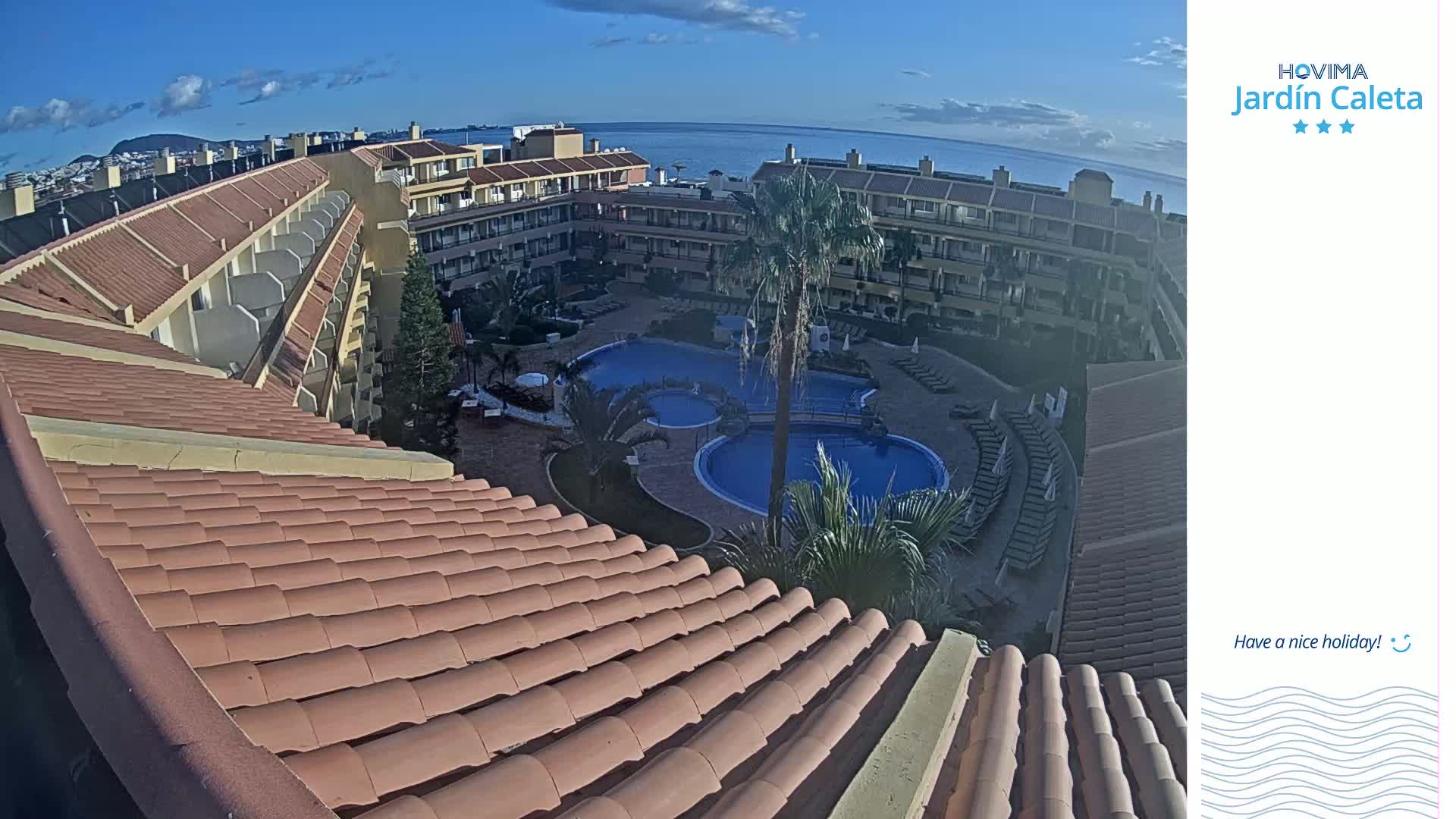 A sunny day overlooks a resort complex with multiple buildings surrounding a large, curved swimming pool.