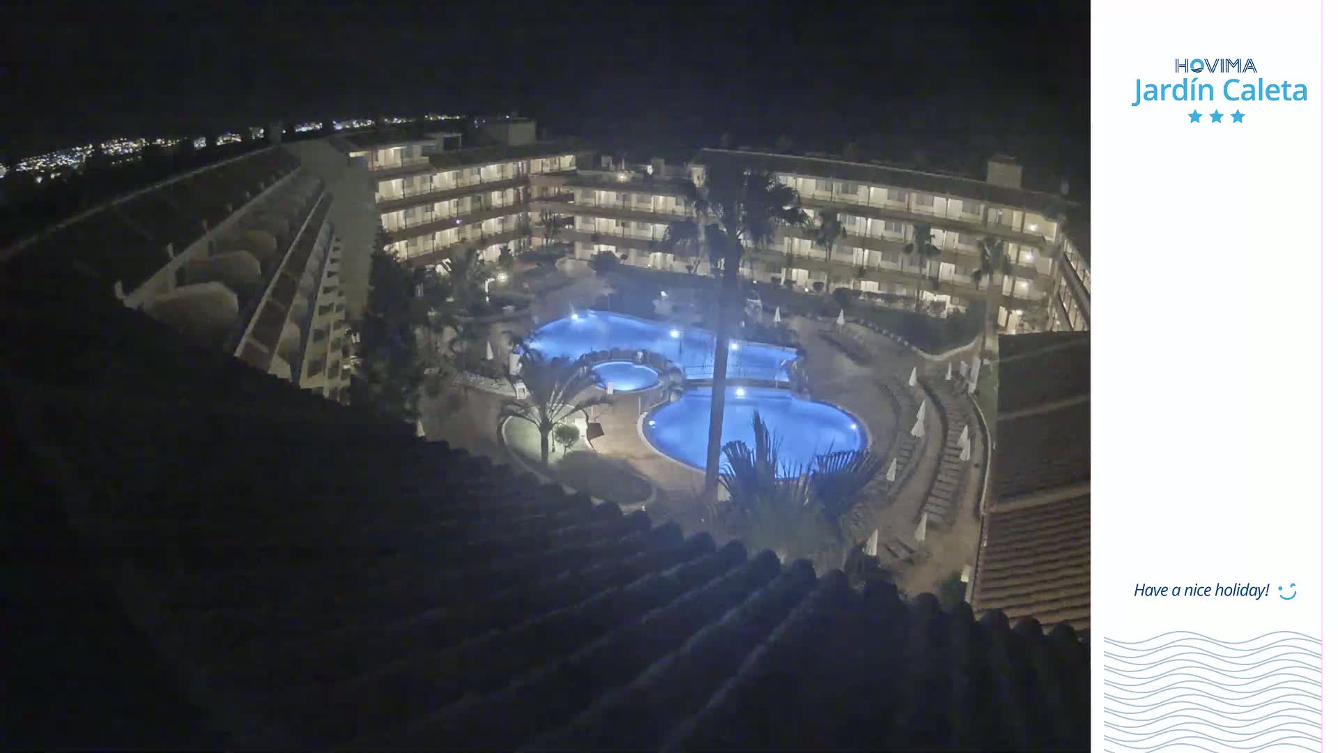 A nighttime aerial view shows a multi-story building complex surrounding a lit-up swimming pool area.