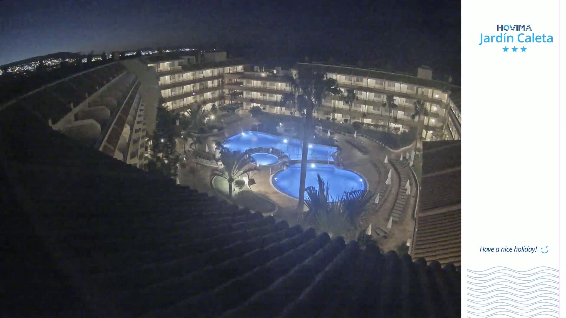 A nighttime aerial view shows a multi-story hotel complex surrounding a lit swimming pool area.