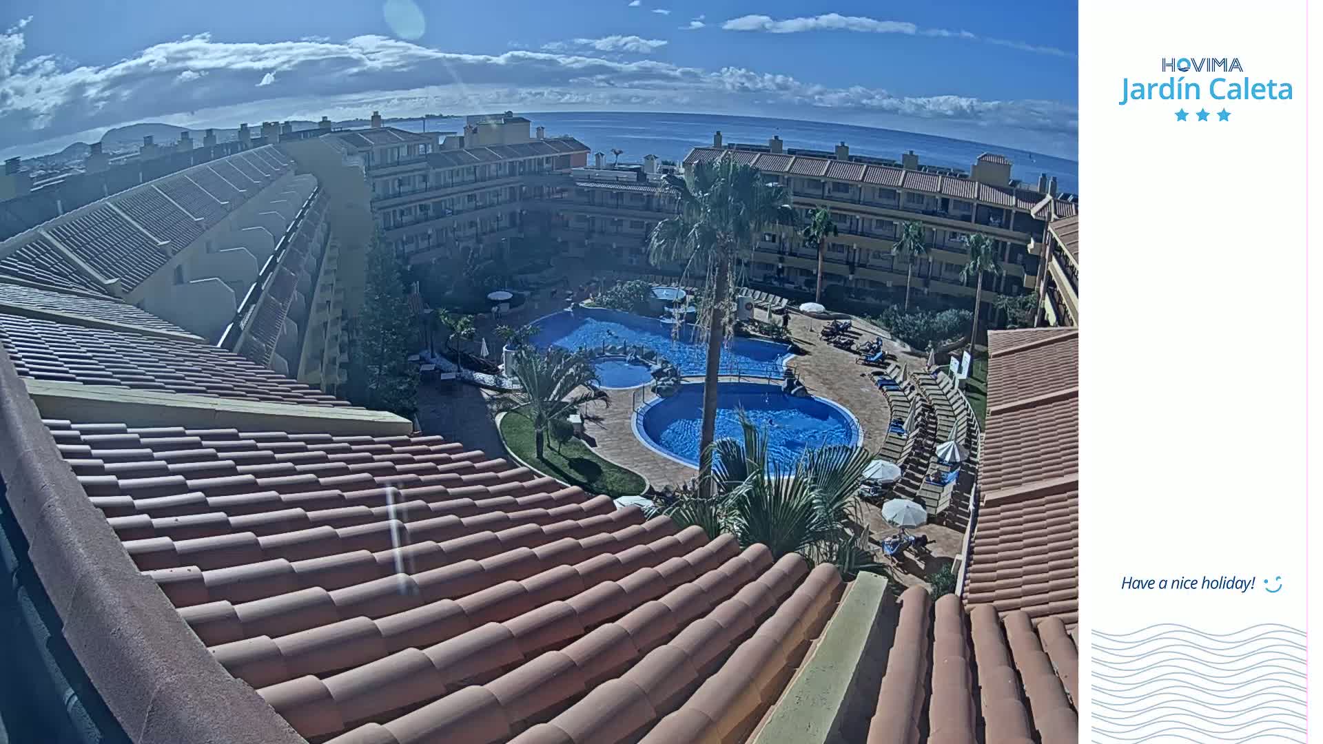 A tiled roof overlooks a courtyard with a swimming pool and surrounding buildings, all under a partly sunny sky.