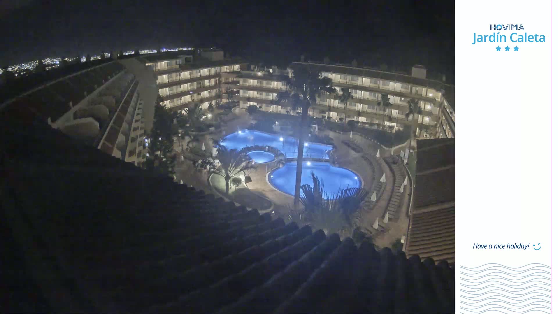 A nighttime aerial view shows a multi-story building complex surrounding a lit-up swimming pool.
