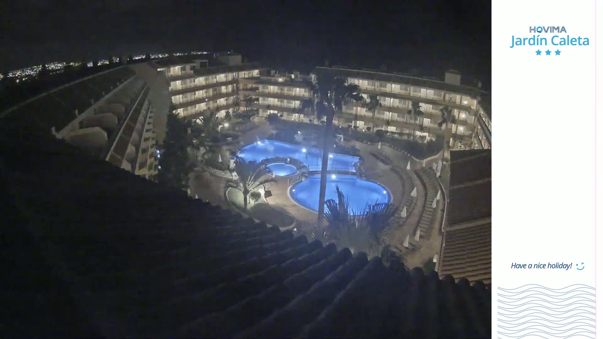 An illuminated resort complex at night, featuring multiple pools surrounded by buildings and palm trees.