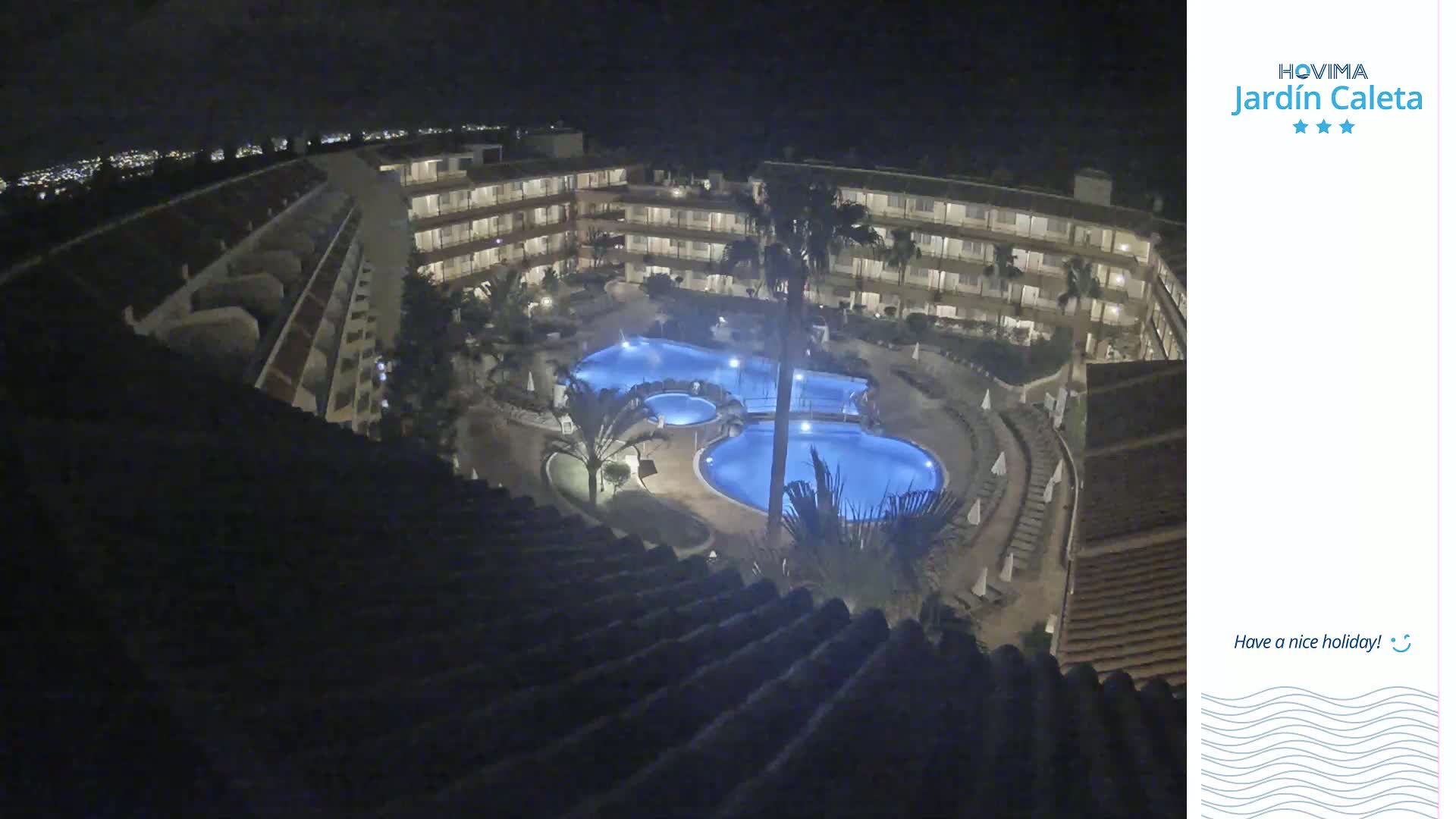 An illuminated, multi-level hotel complex with a pool area is seen at night.