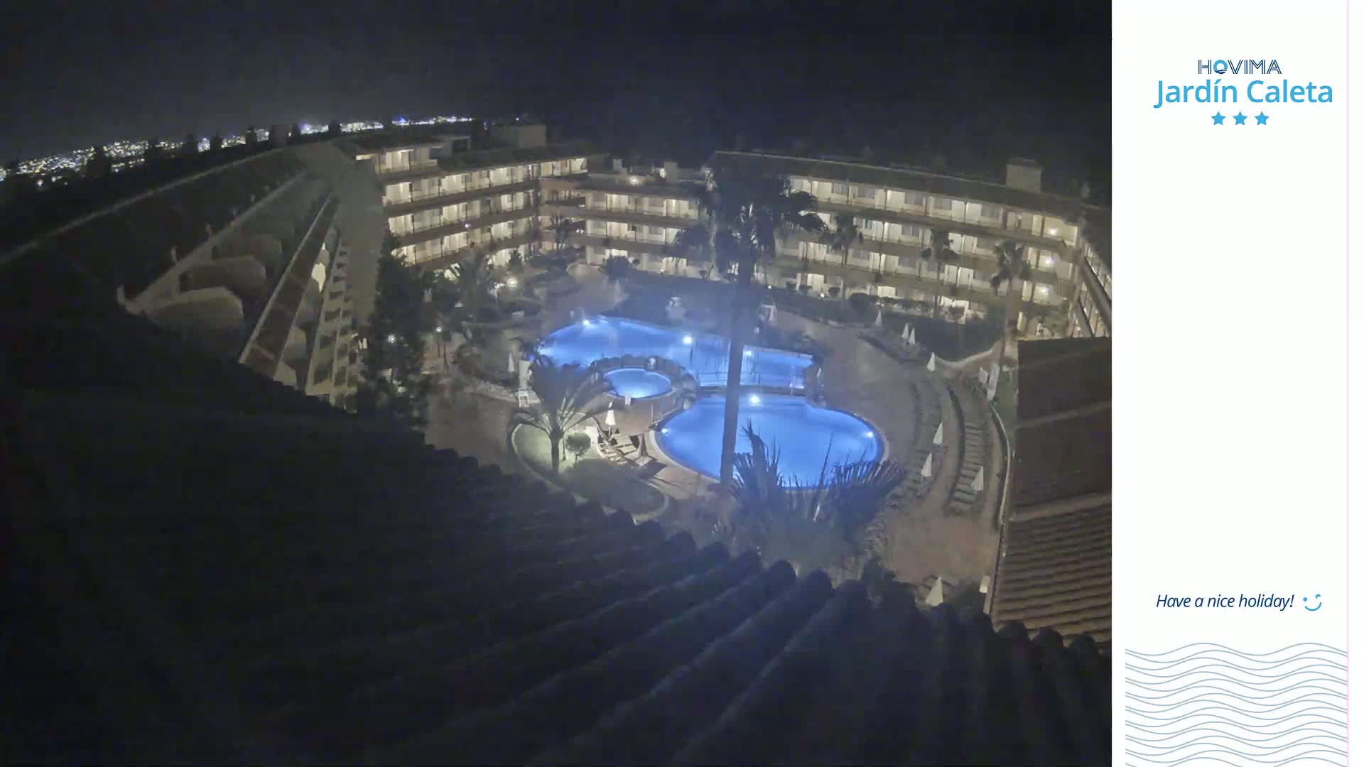 A nighttime overhead view of a multi-story building complex with a lit-up swimming pool in the courtyard.