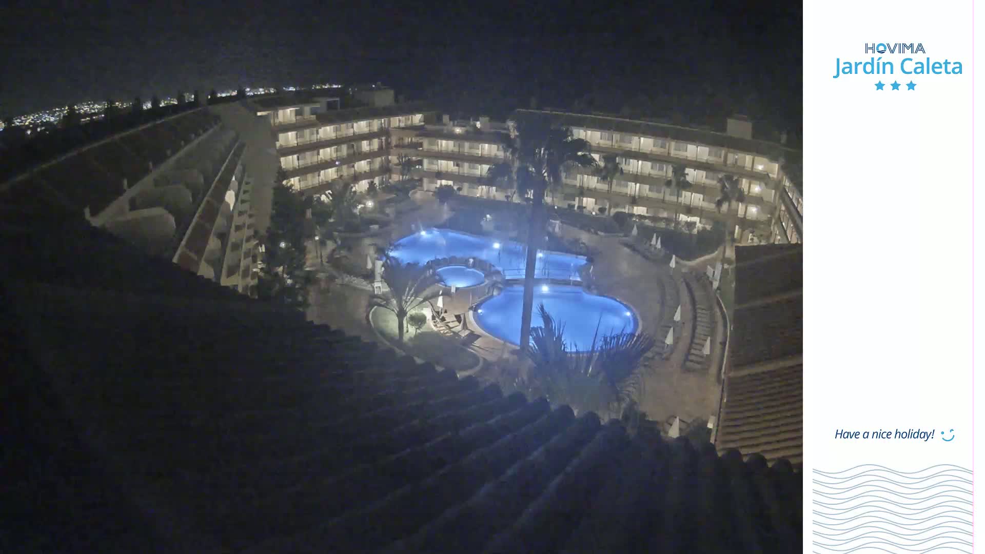 A nighttime aerial view shows a multi-story hotel complex surrounding a lit swimming pool area.