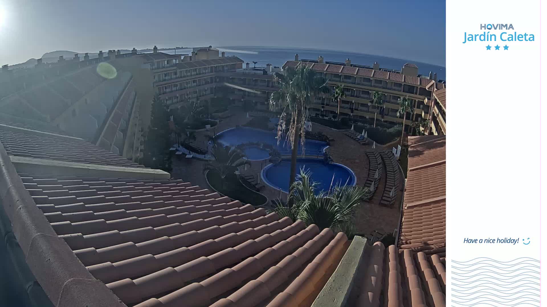 A sunny view from a rooftop overlooking a resort complex with multiple swimming pools and a clear ocean in the distance.
