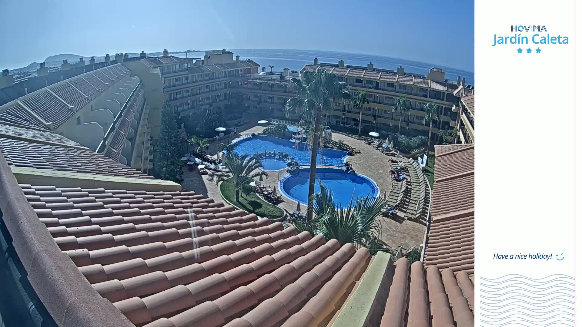 A sunny day overlooking a resort's courtyard with multiple pools surrounded by buildings and palm trees.