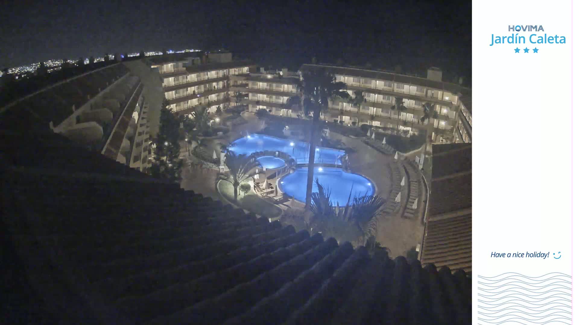 A nighttime aerial view shows a multi-story resort complex surrounding a lit swimming pool.