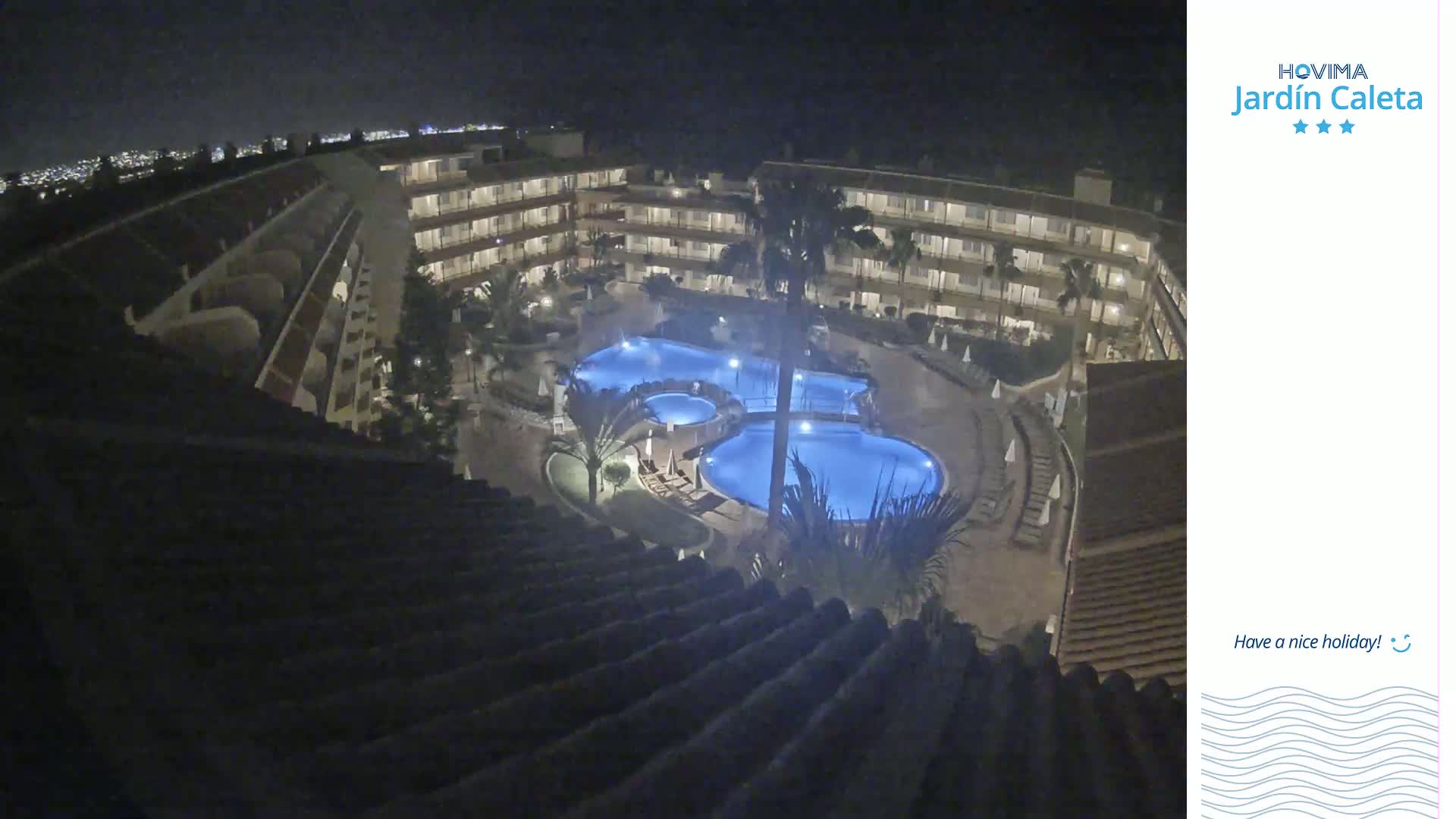 A nighttime, high-angle view shows a multi-story hotel complex surrounding a lit, kidney-shaped swimming pool.
