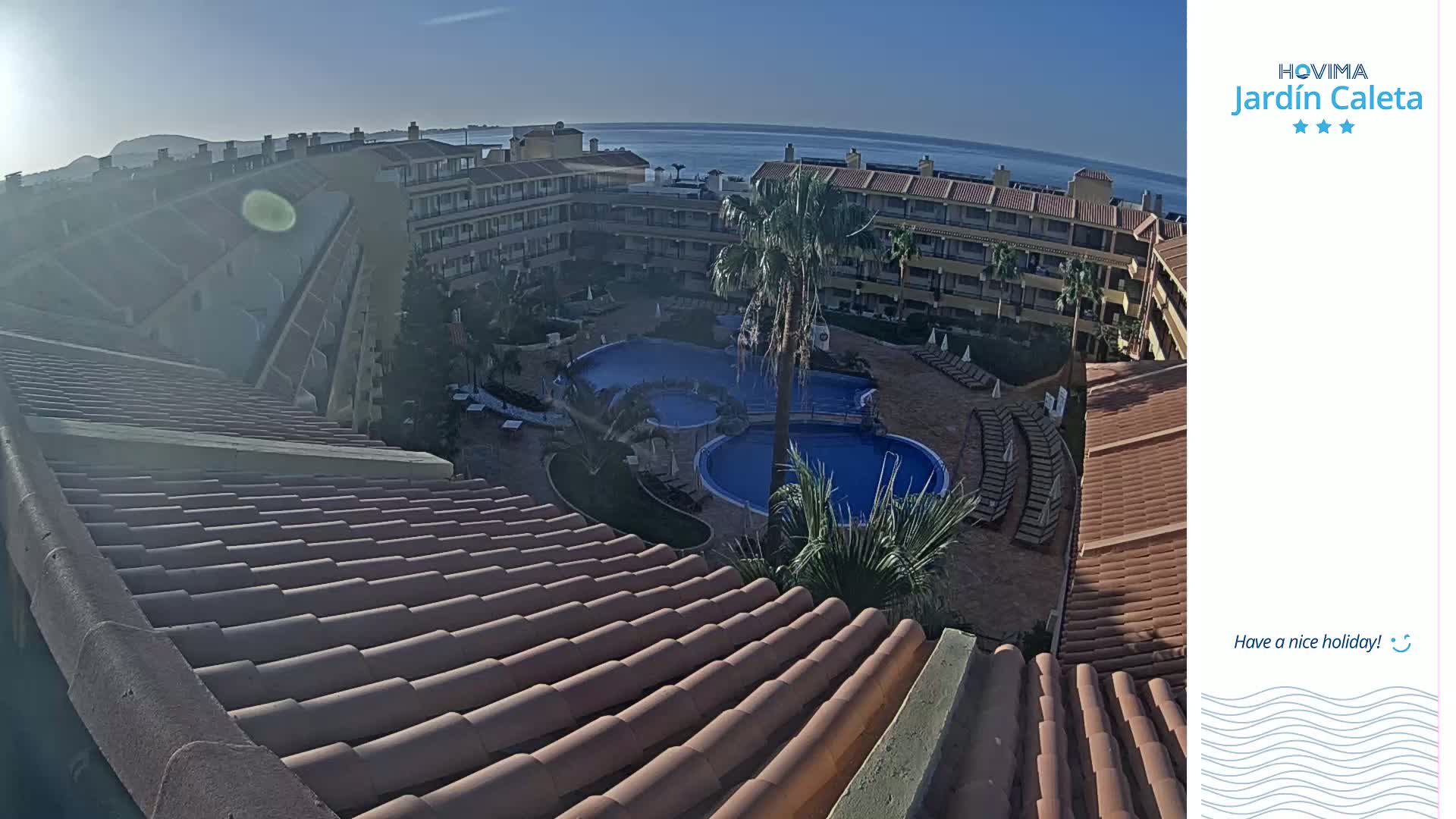 A sunny view overlooking a resort complex with multiple pools, surrounding buildings, and a distant ocean.