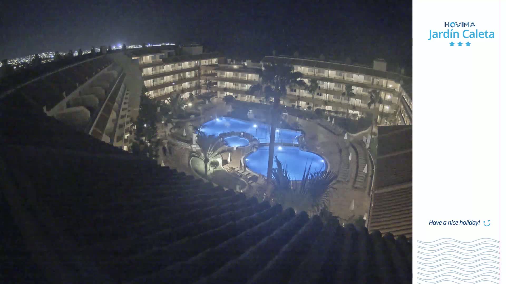 A nighttime aerial view shows a multi-story hotel complex with illuminated swimming pools.