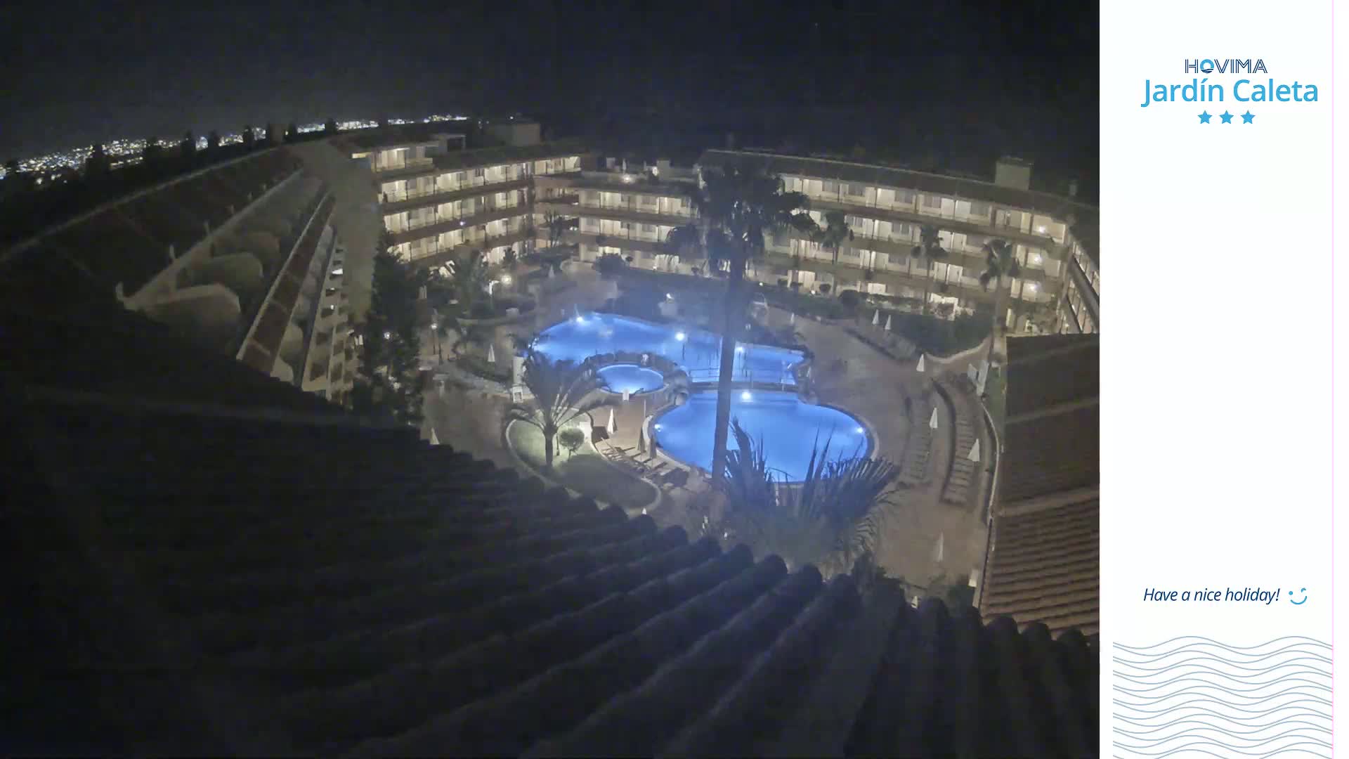 A nighttime view of a multi-story building complex surrounding a lit swimming pool.