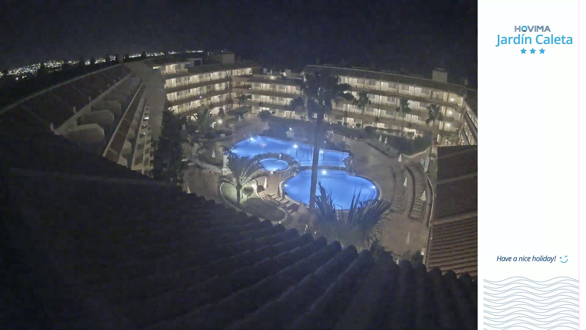 A nighttime aerial view shows a multi-story hotel complex surrounding a lit swimming pool area.