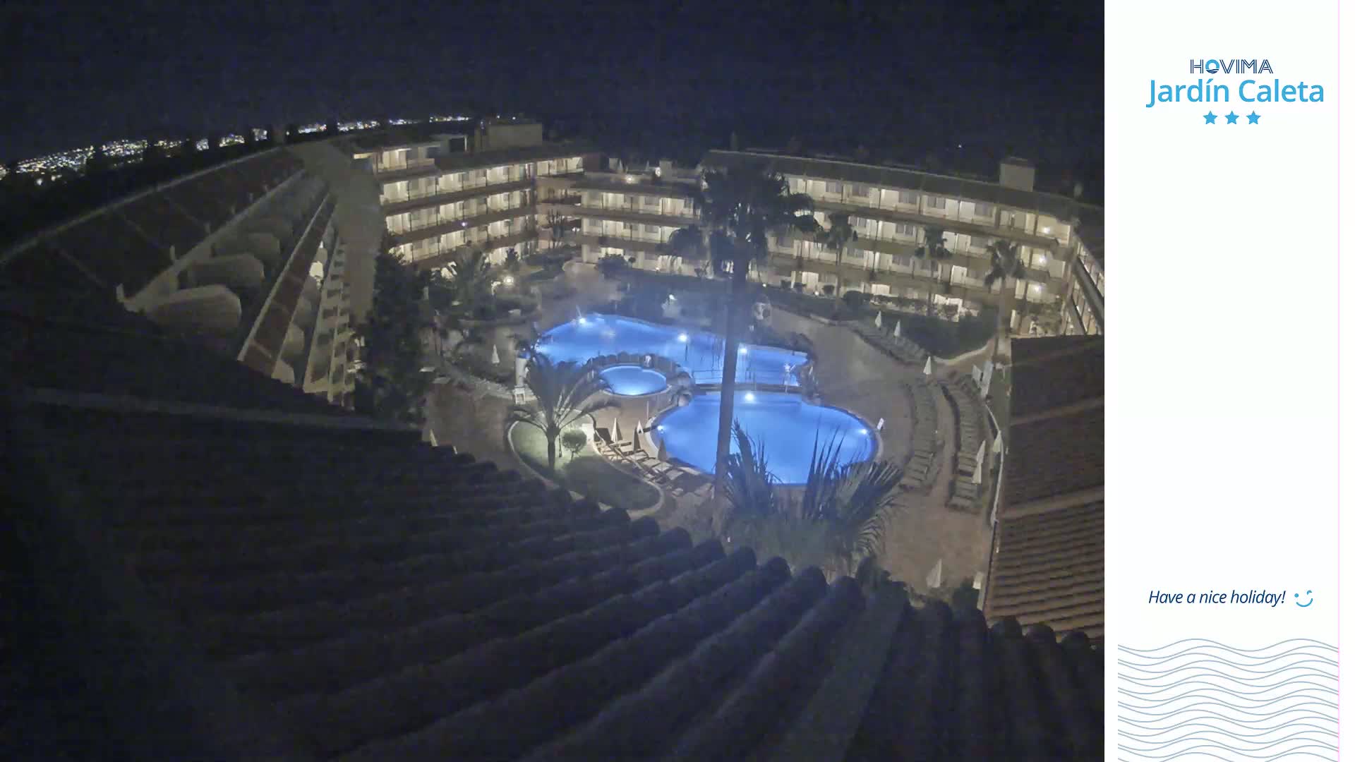 A nighttime, overhead view shows a multi-story building complex surrounding a lit swimming pool area.