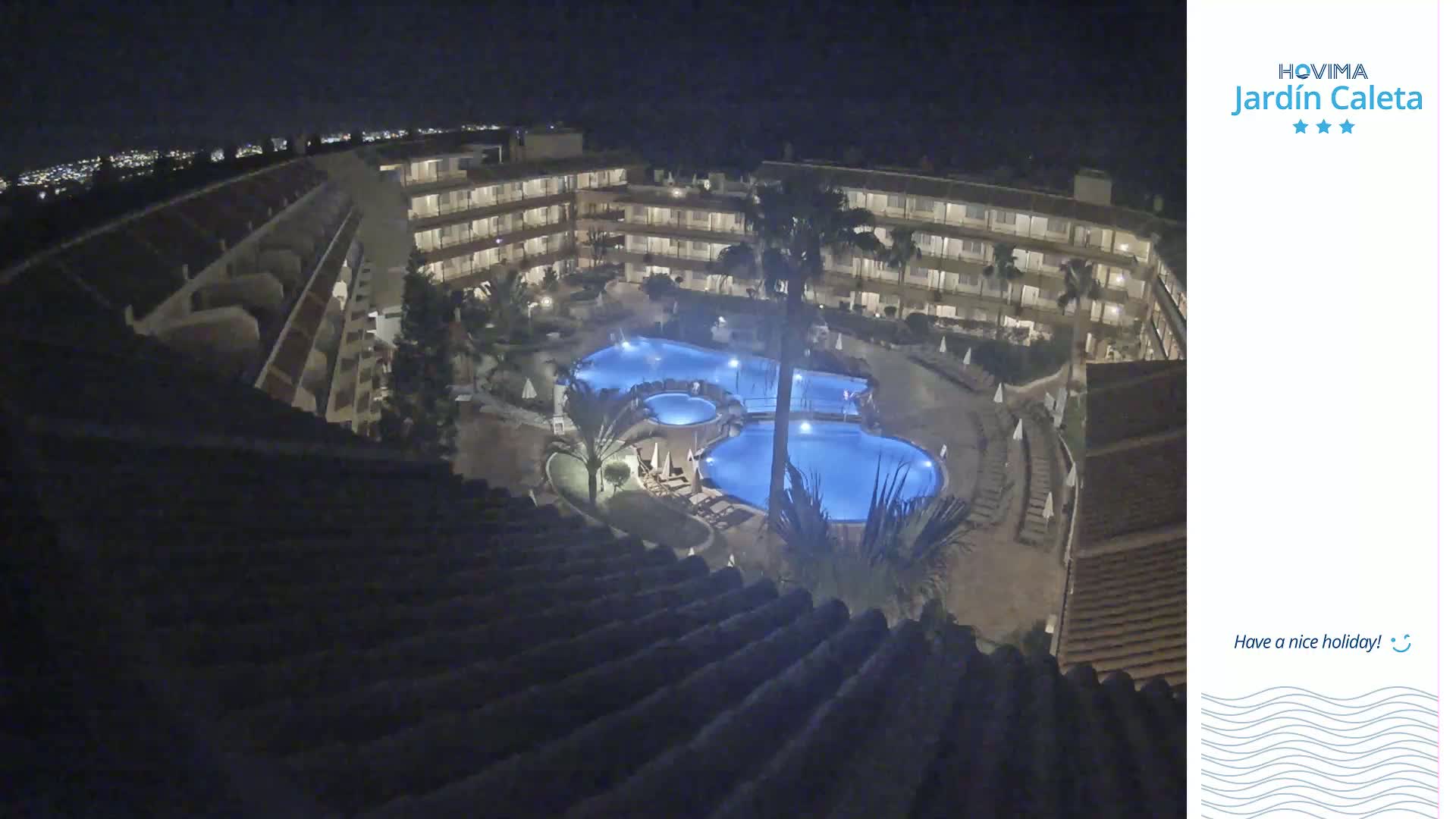 An illuminated resort pool complex is surrounded by a multi-story building at night.