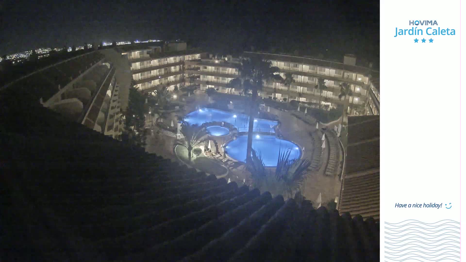 A nighttime view of a multi-story hotel complex with illuminated pools surrounded by landscaping.