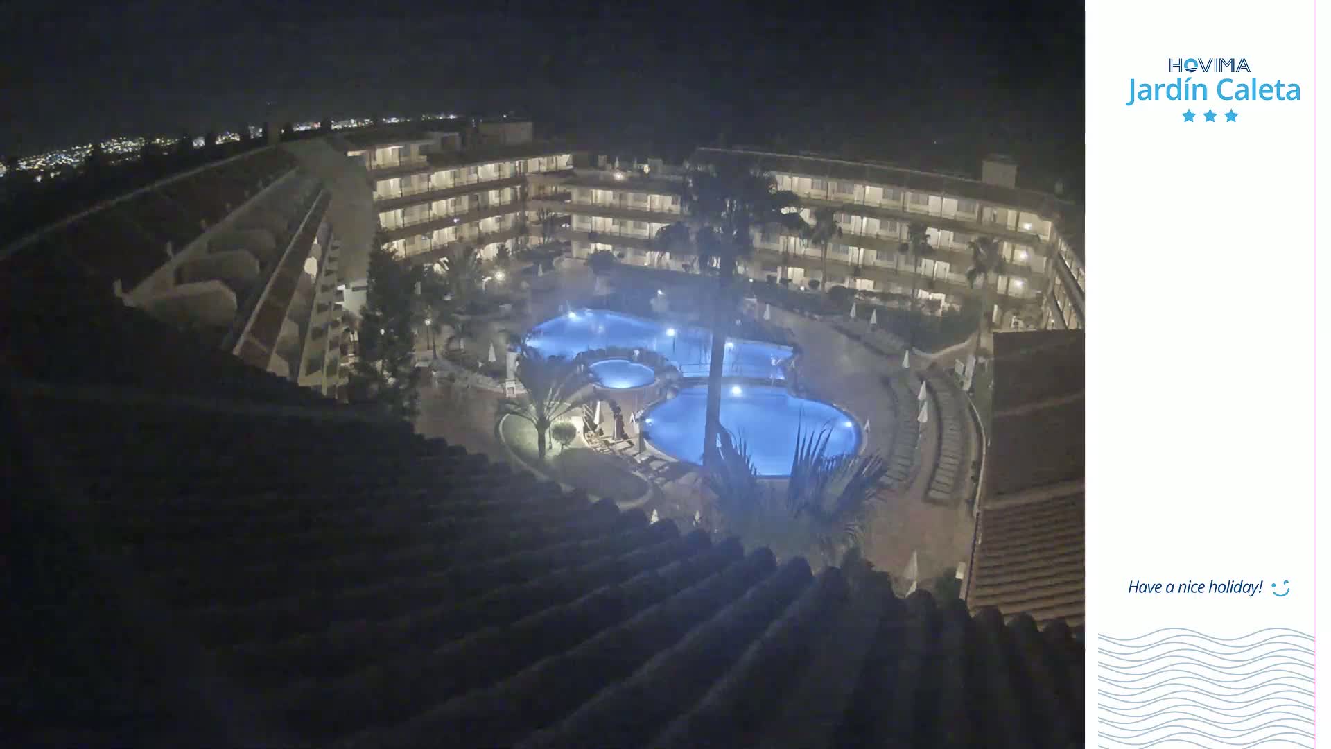 A nighttime aerial view shows a multi-story building complex surrounding a lit-up swimming pool.