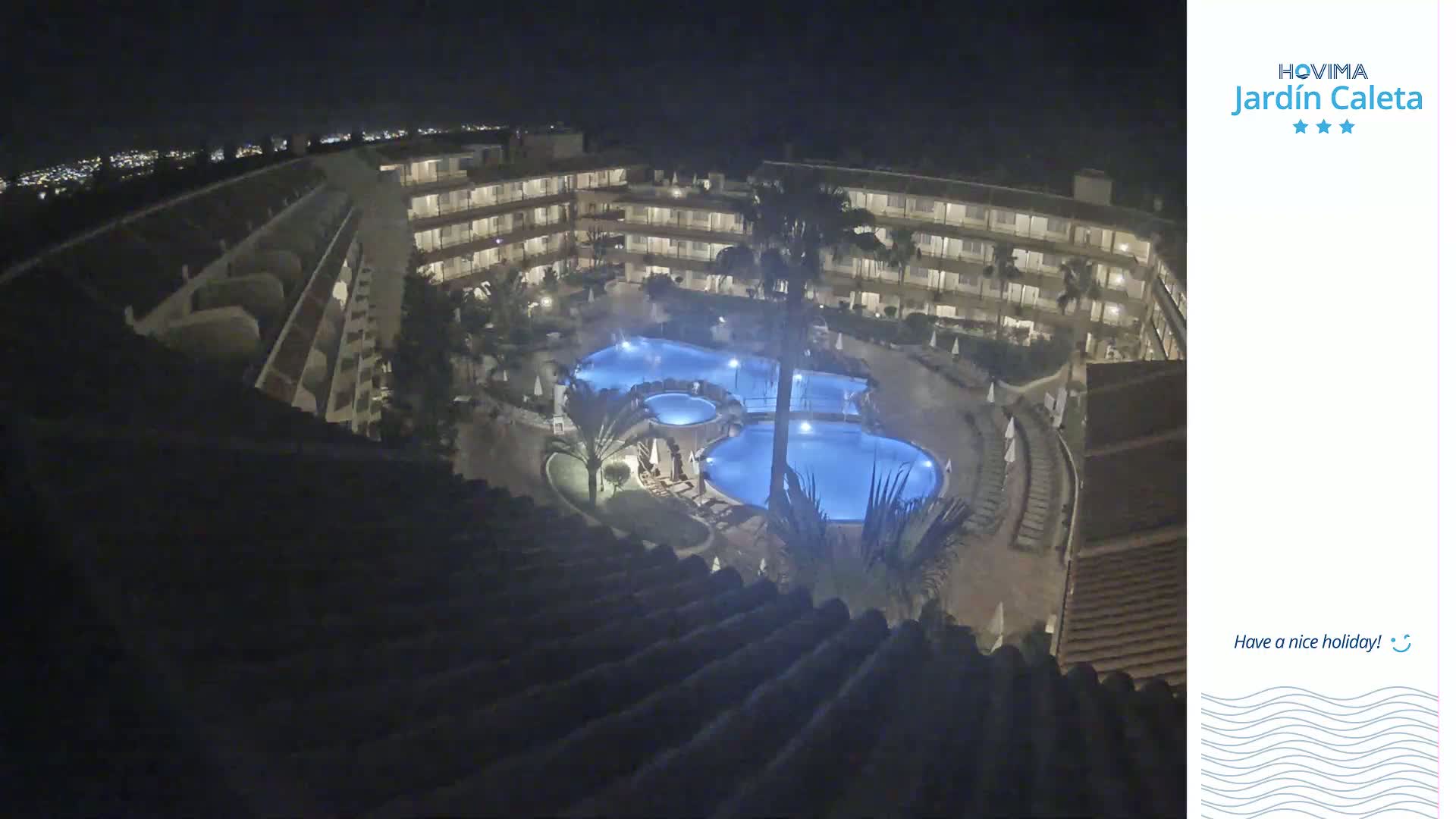 A nighttime aerial view shows a multi-story hotel complex surrounding a lit swimming pool.