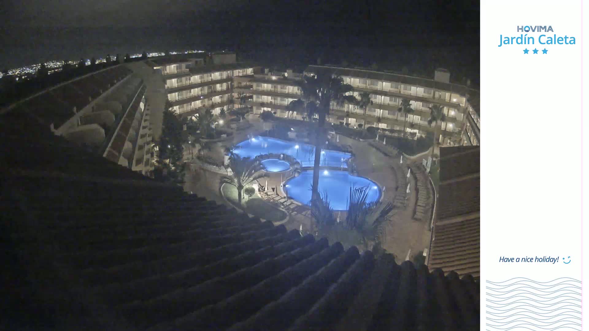 A nighttime aerial view shows a multi-story hotel complex surrounding a lit swimming pool area.