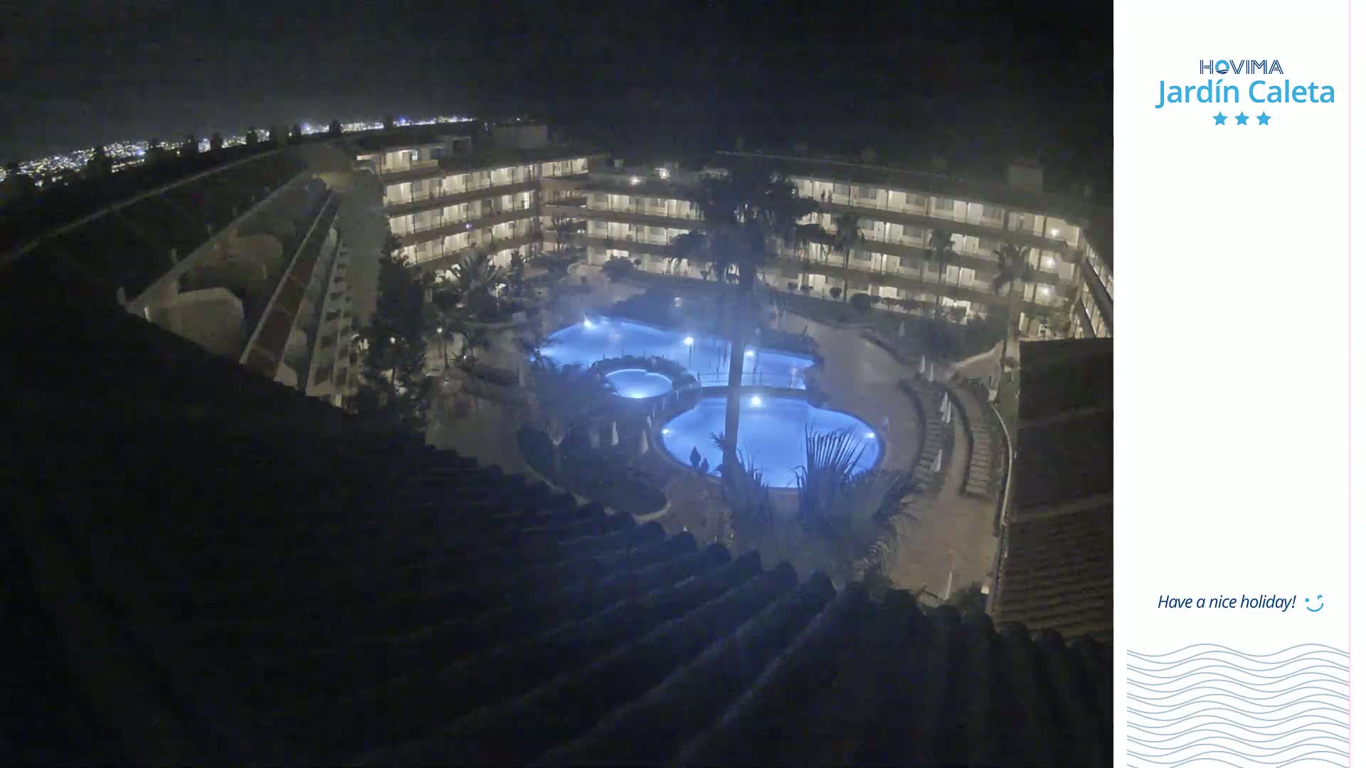 A nighttime, overhead view shows a multi-story building complex surrounding a lit swimming pool area.