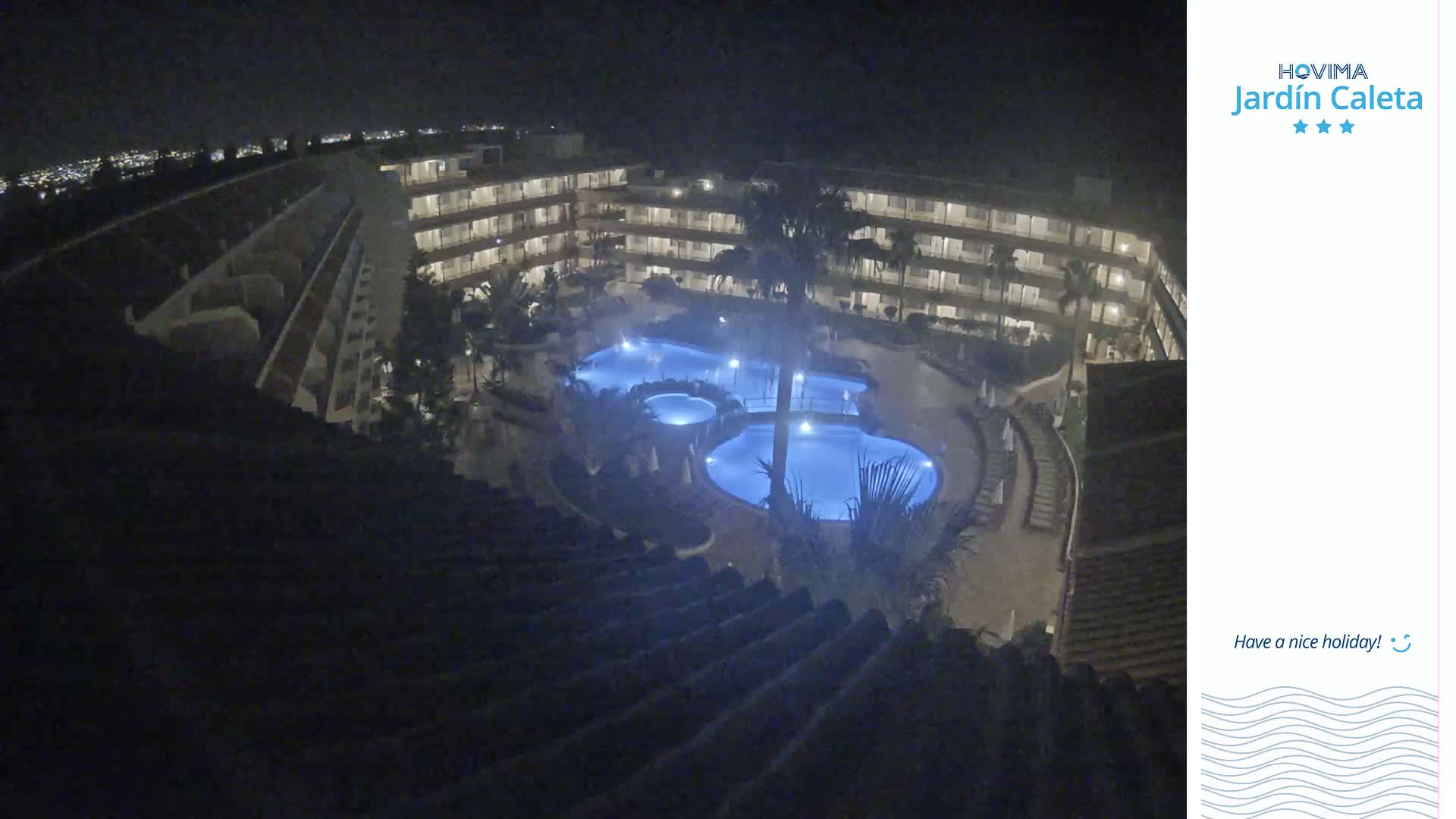 A nighttime, aerial view shows a multi-story building complex surrounding a lit, multi-section pool.