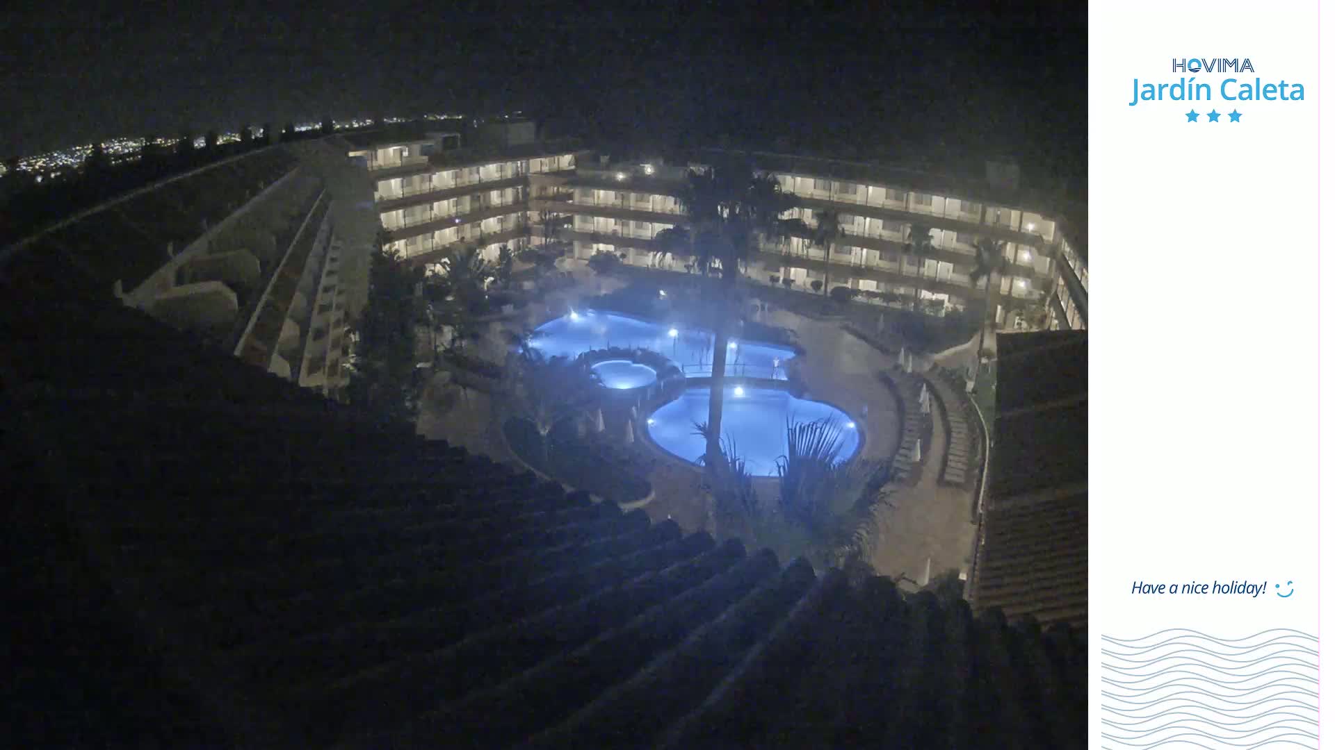 A nighttime, high-angle view shows a multi-story building surrounding a lit-up pool complex.