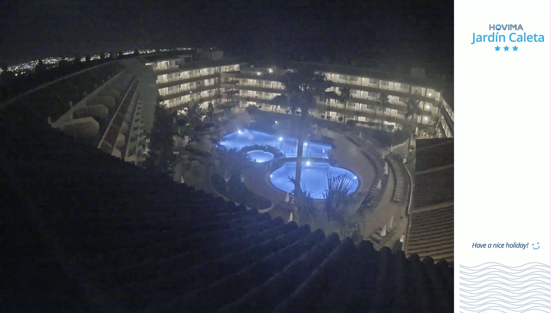 A nighttime aerial view shows a multi-story building complex surrounding a lit-up swimming pool area.