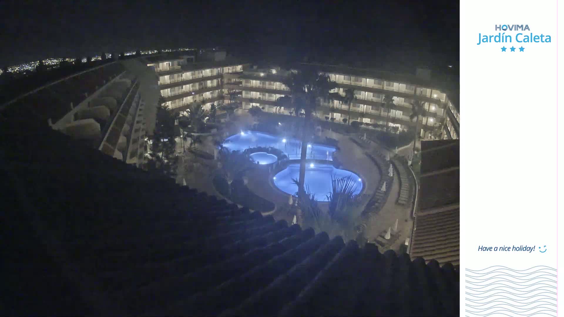 A nighttime aerial view shows a multi-story building complex surrounding a lit swimming pool.