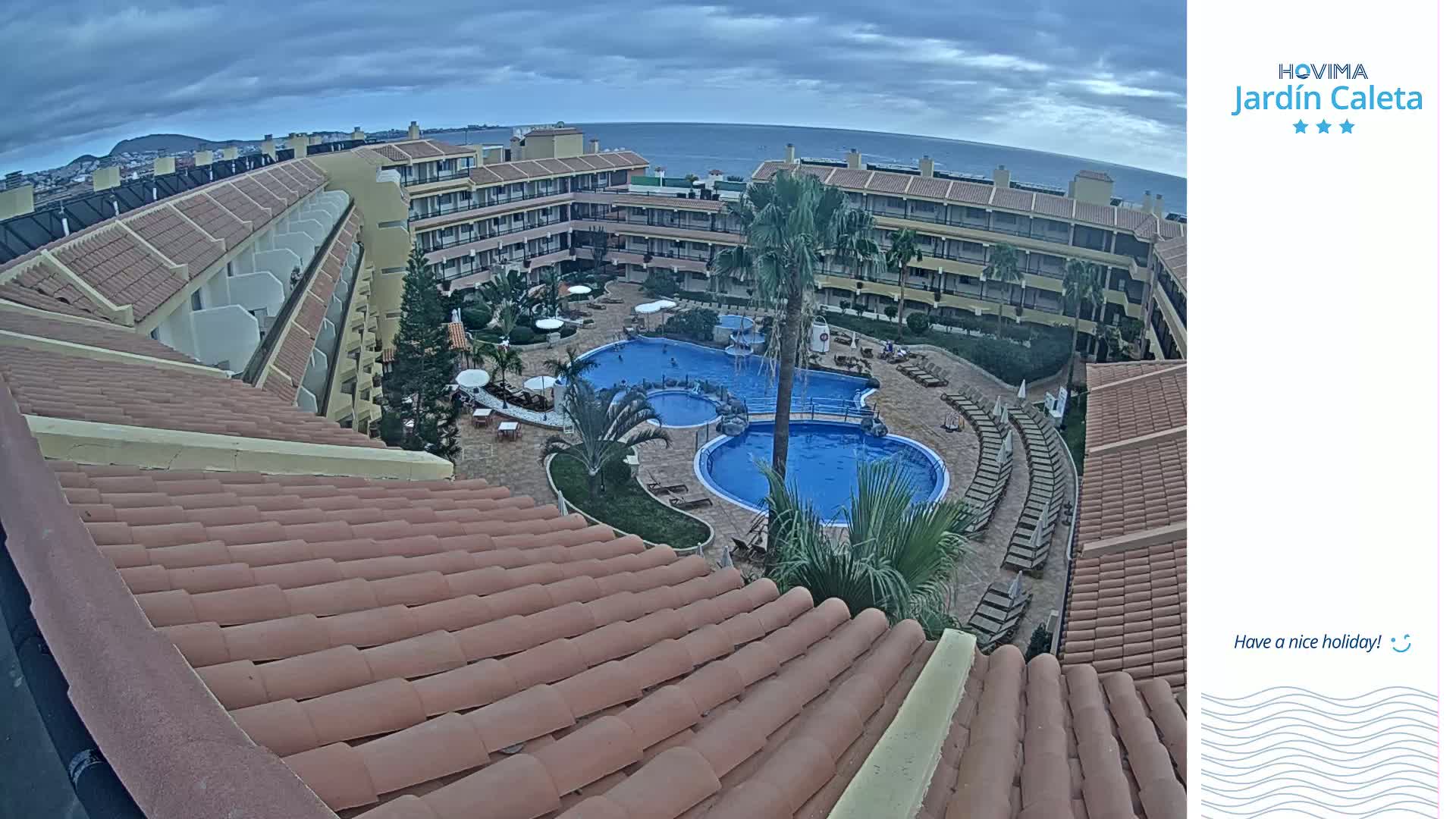 An overhead view of a resort pool area with multiple buildings and a tiled roof in overcast conditions.