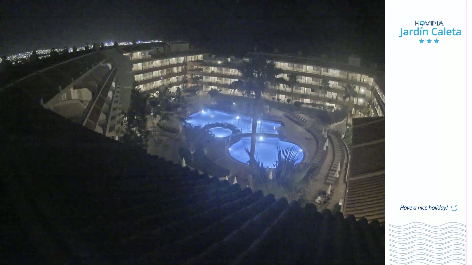 A nighttime, overhead view of a multi-story building complex surrounding illuminated swimming pools.