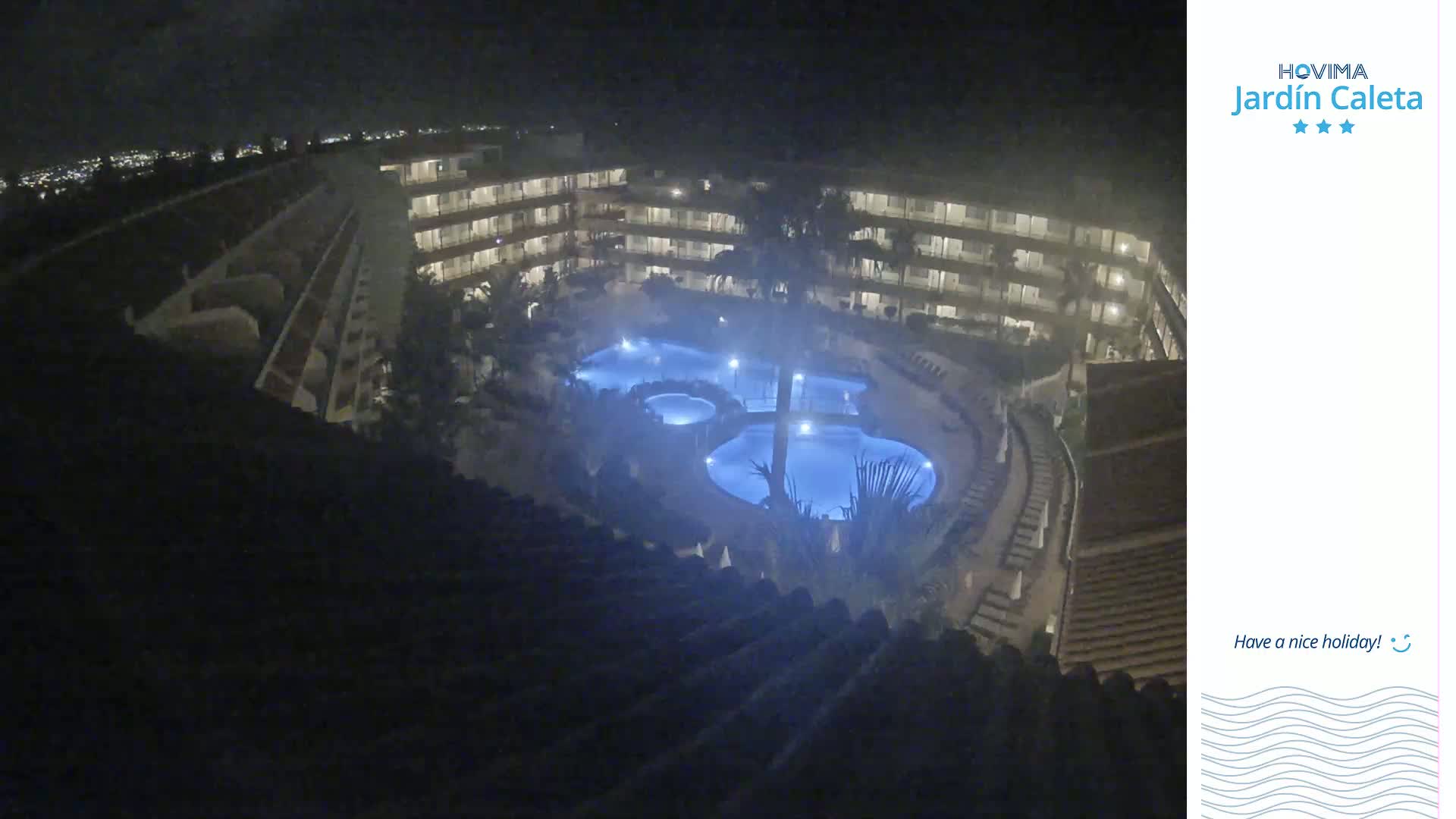 A nighttime, aerial view shows a multi-story building complex surrounding a lit swimming pool area.